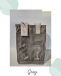 Gray canvas wine bag with a wine linocut print on the left side pocket and a wine glass linocut print on the right side pocket. The front view features 3 pockets, the back also has 3 pockets. It has a seed paper bag from moodwestudio tied to the beige handle. 